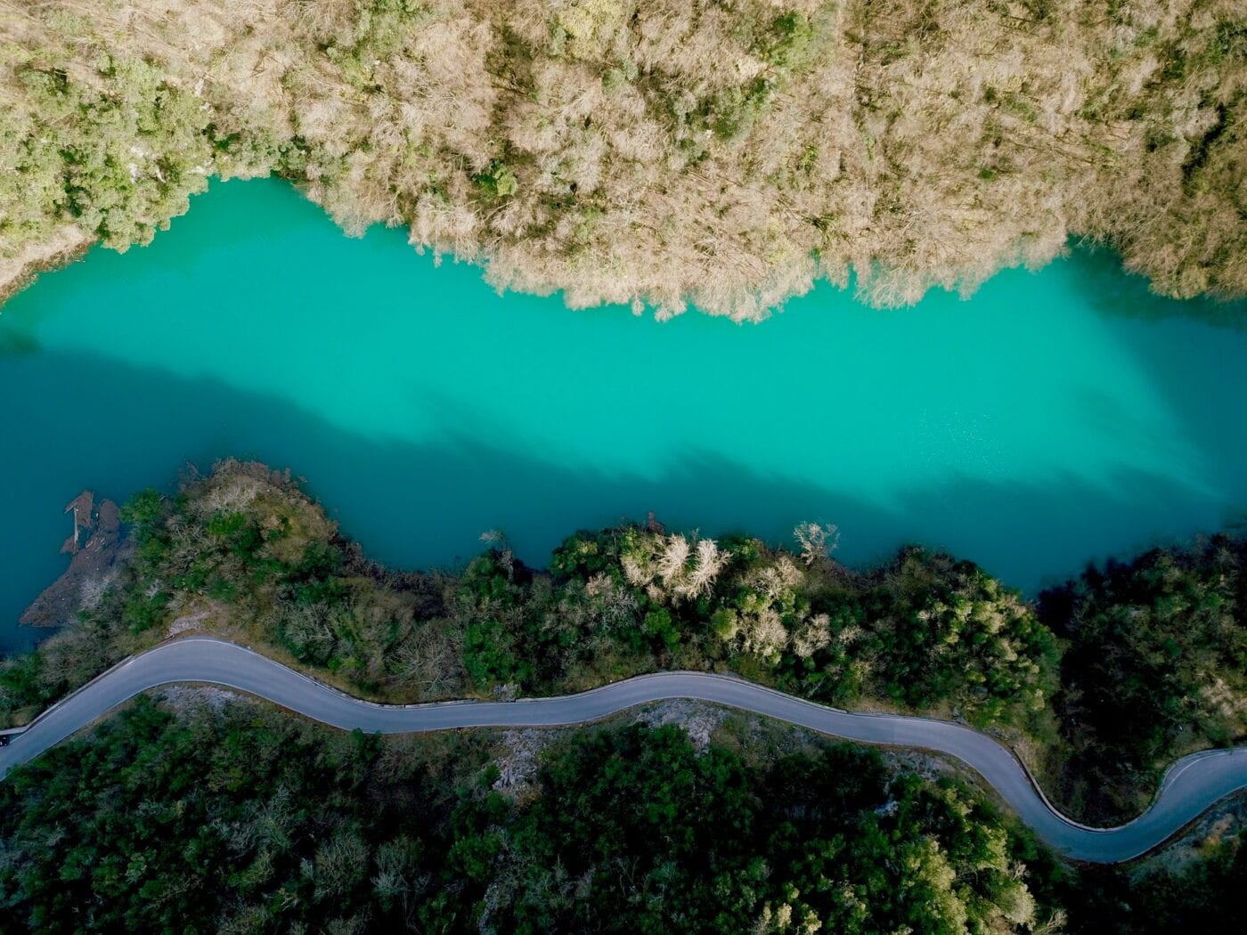 Aerial view of a winding road along a turquoise river surrounded by dense forest